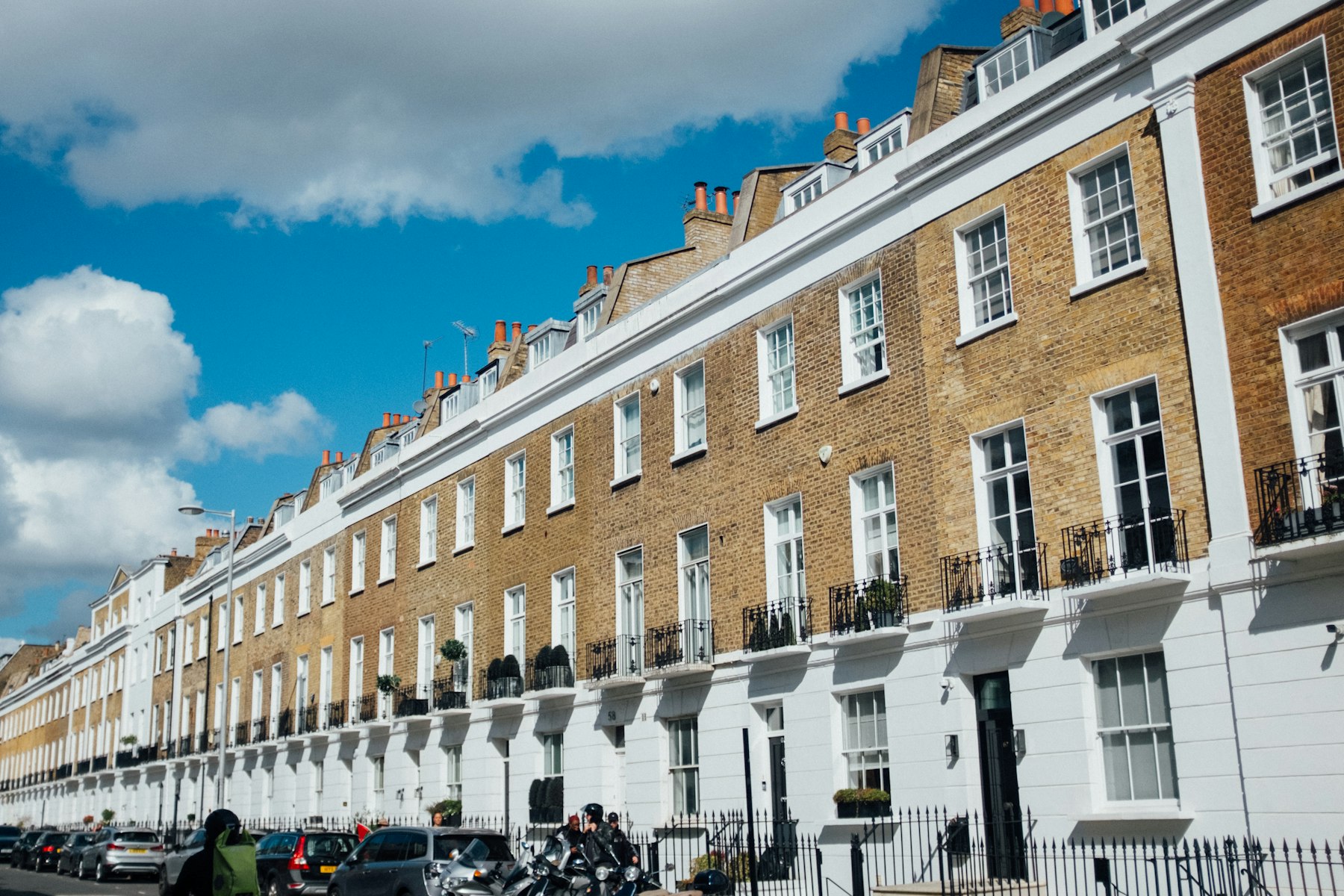 A row of traditional Georgian-style terraced houses with brick facades and white window surrounds under a blue sky